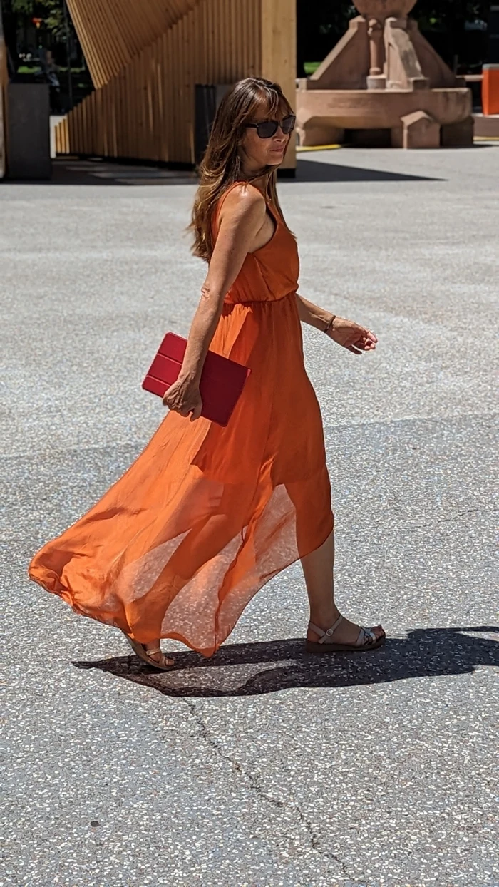 Gudrun Öchsl geht im orangefarbenen Kleid mit einem Tablet in der Hand
